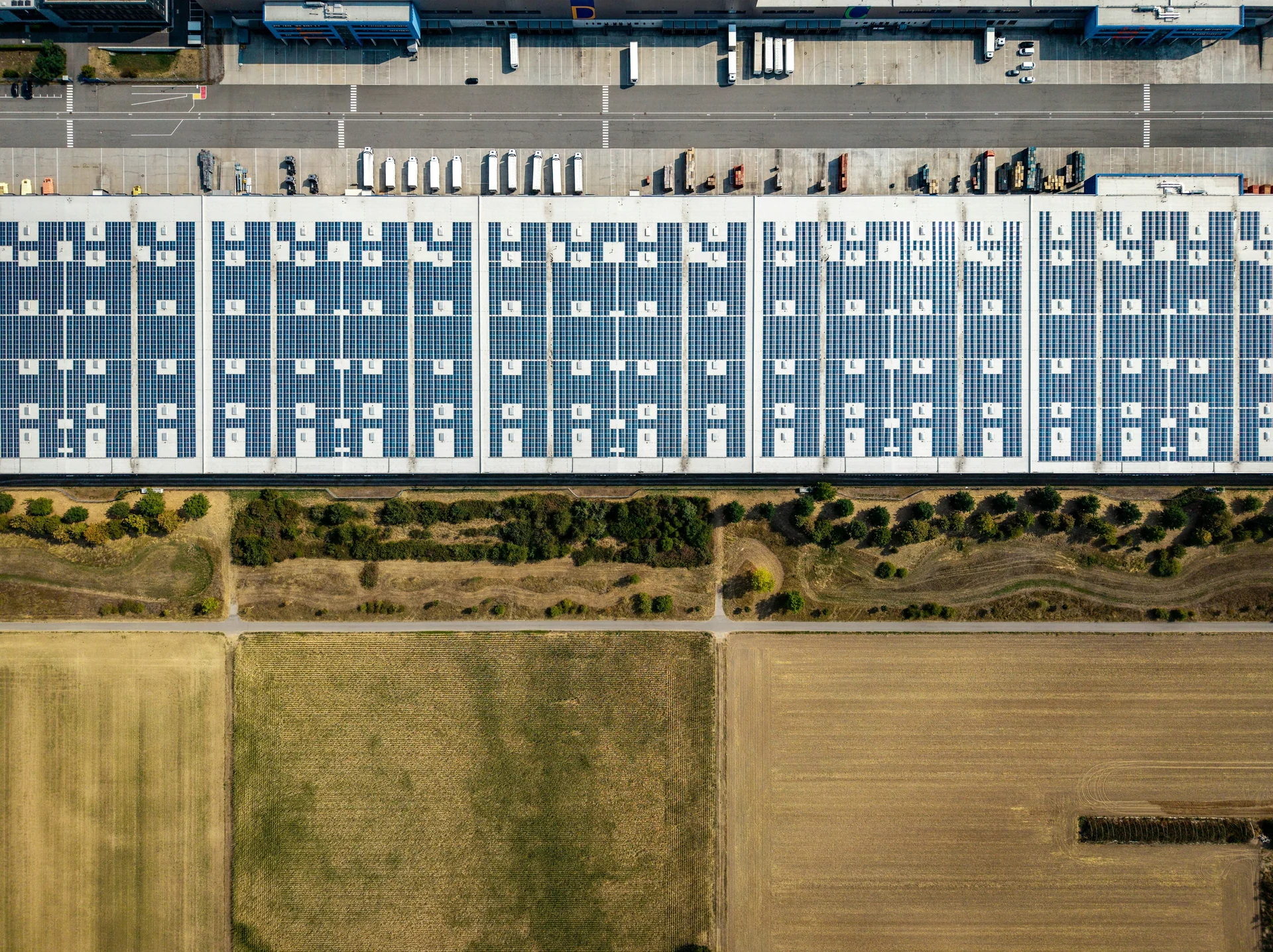 Overhead view of warehouse rooftop solar panels beside loading docks and trucks